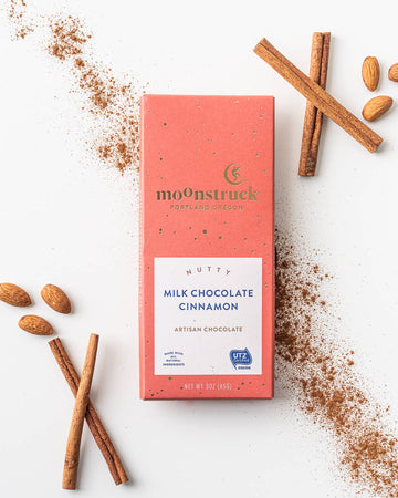 Moonstruck Milk Chocolate Cinnamon bar with cinnamon sticks and ground cinnamon on a white background