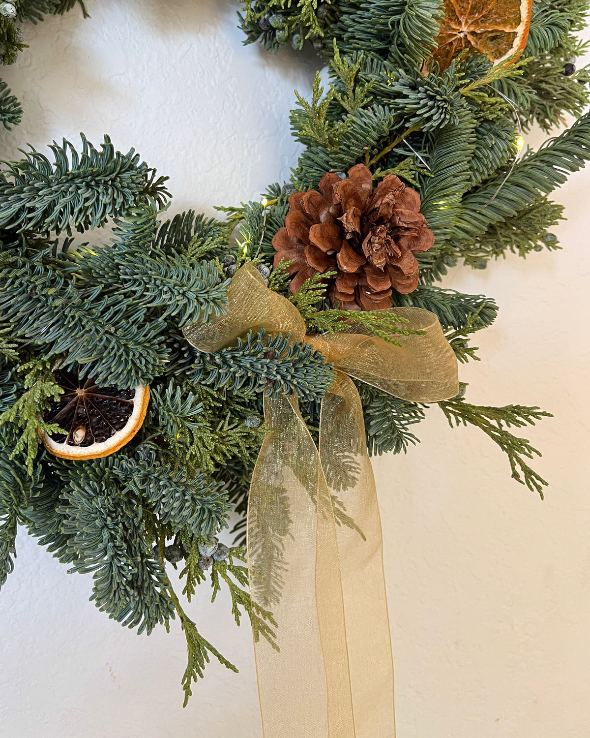 Christmas wreath with greenery, pinecones, and gold ribbon on a white background