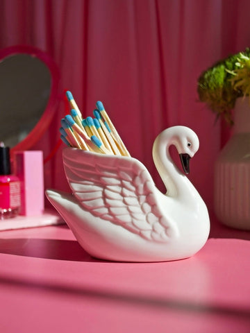 White swan-shaped match holder with matches on a pink surface