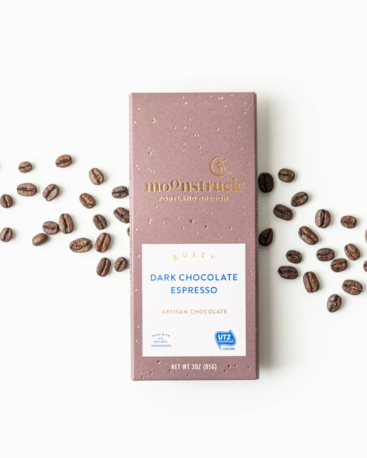 Moonstruck Dark Chocolate Espresso bar with scattered coffee beans on a white background