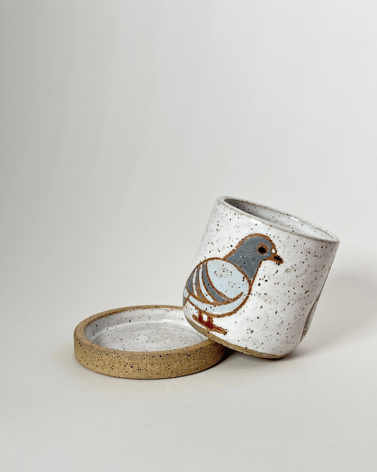 Speckled ceramic cup with a bird design on a light gray background