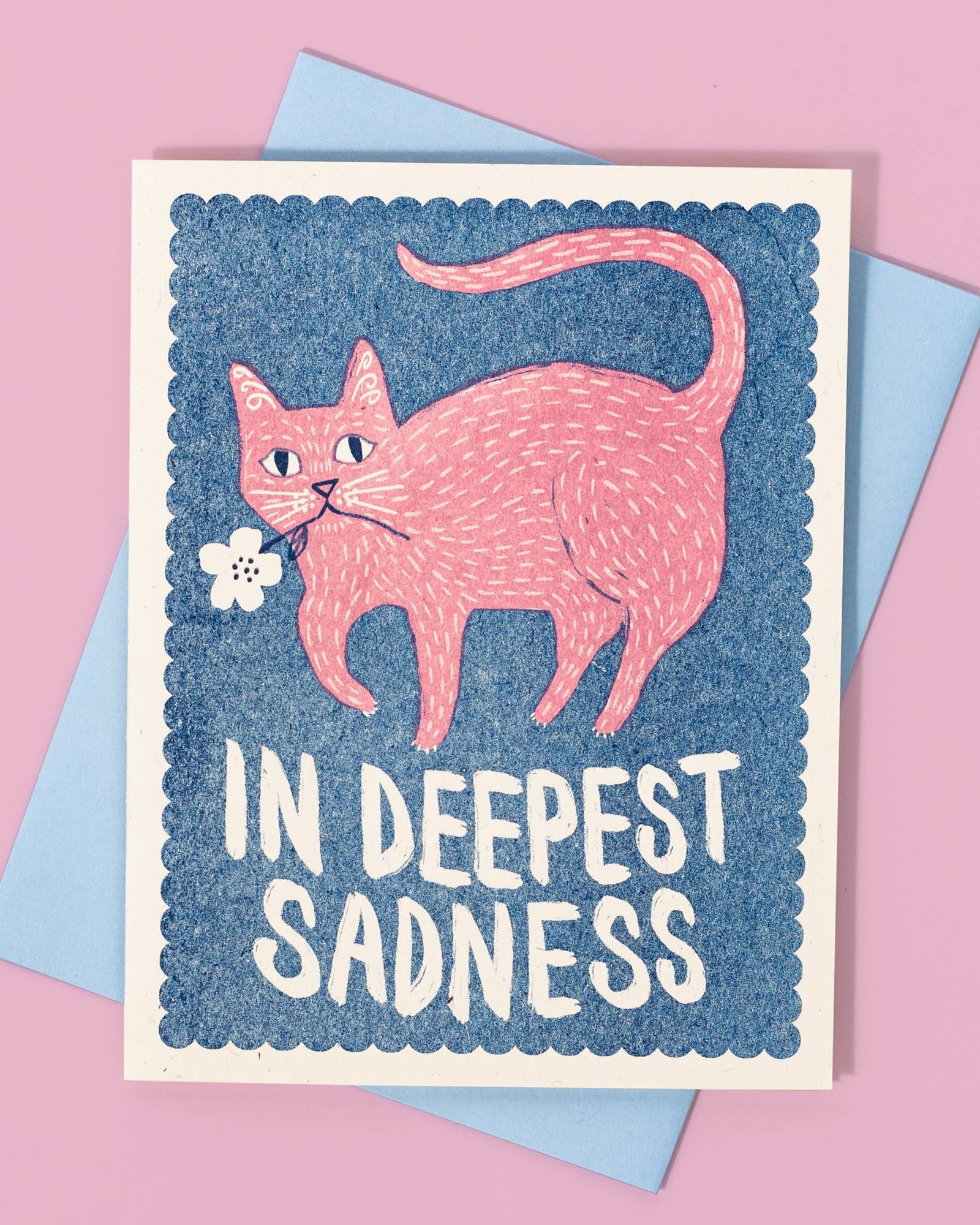 A folded risograph card with a blue background, featuring an illustration of a cat with a flower, and the text 'In Deepest Sadness'.