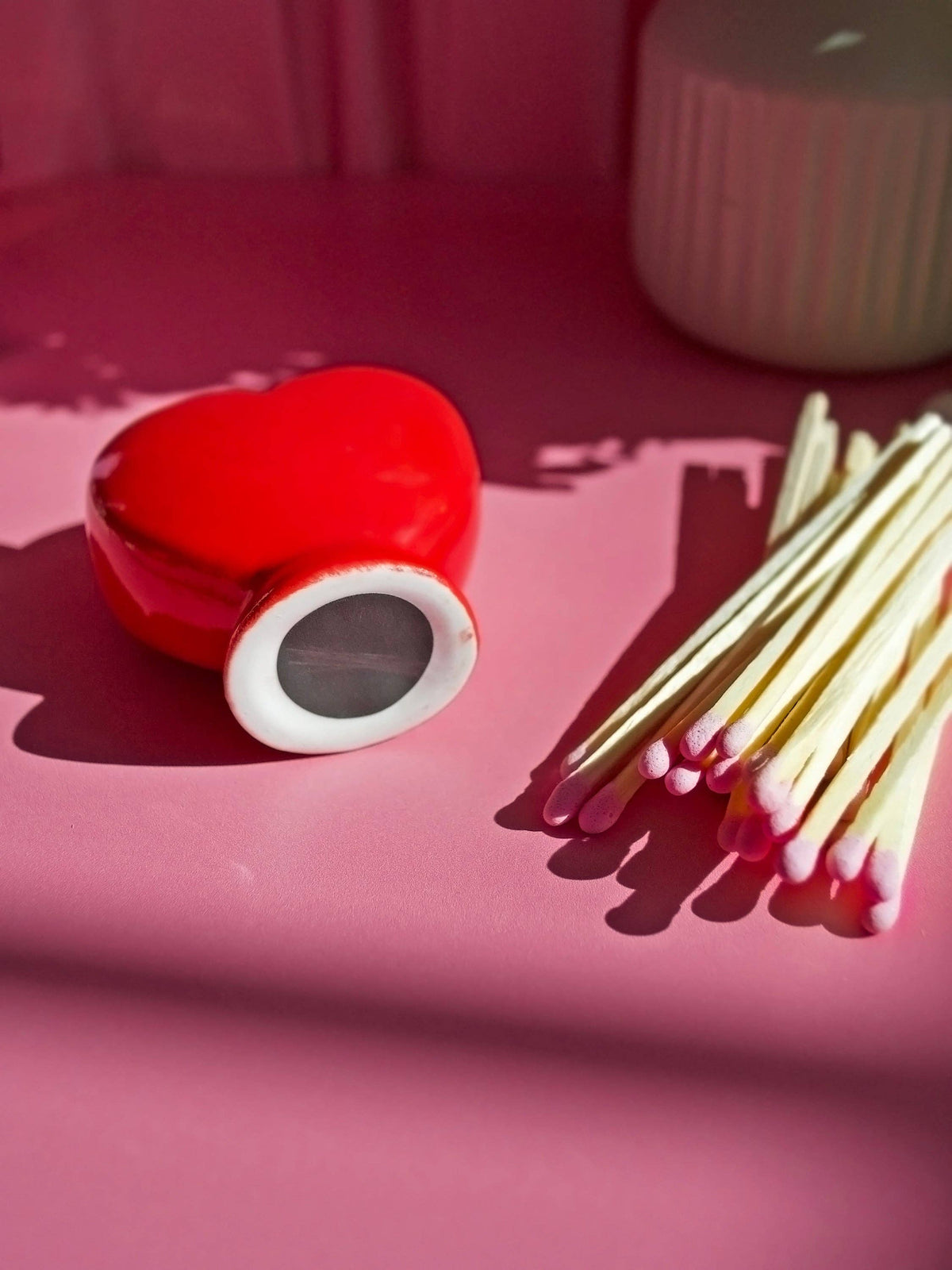 Red heart-shaped match holder with matches on a pink surface