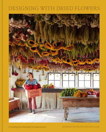 Book cover of 'Designing with Dried Flowers' featuring a person in a flower shop with dried flowers hanging above.