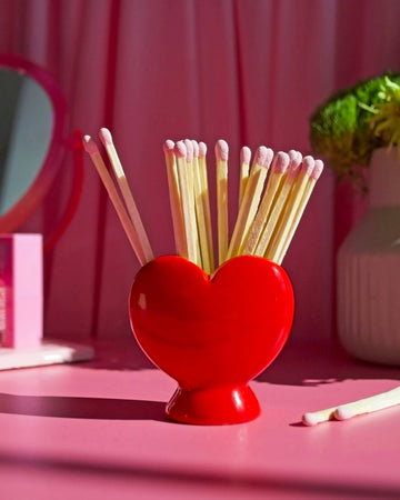 Red heart-shaped match holder with matches on a pink background