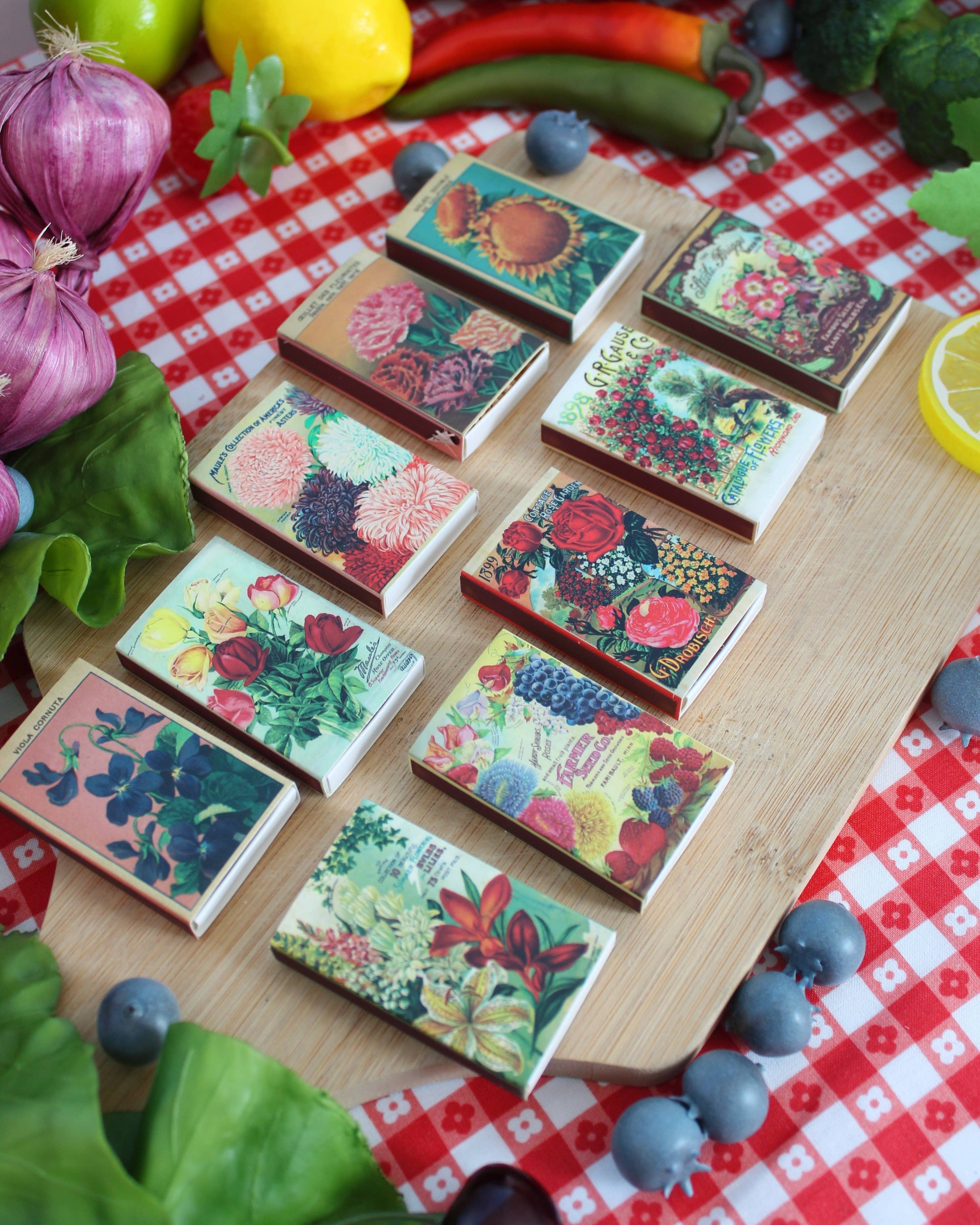 Decorative matchbooks with floral designs on a wooden board over a red and white checkered tablecloth.