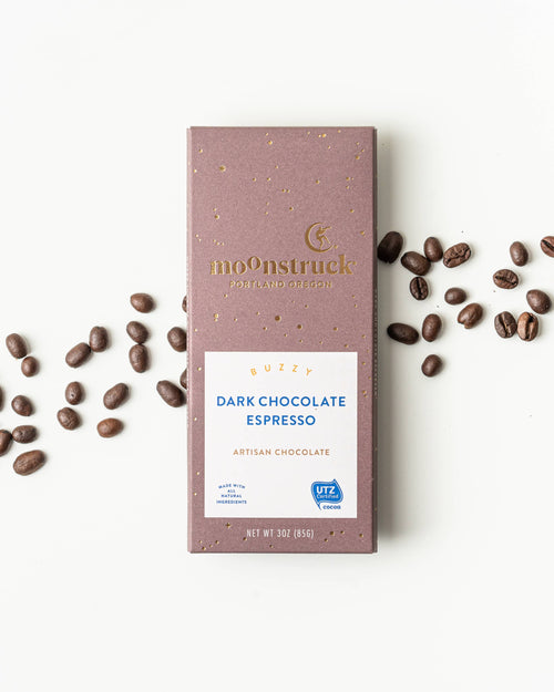 Moonstruck Dark Chocolate Espresso bar with scattered coffee beans on a white background