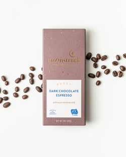 Moonstruck Dark Chocolate Espresso bar with scattered coffee beans on a white background