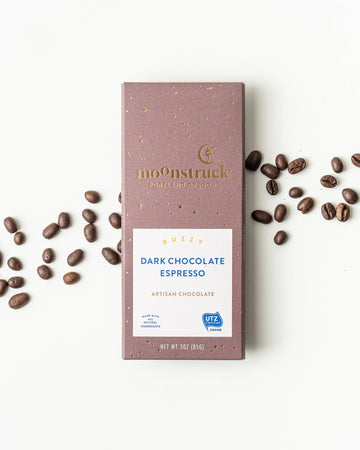 Moonstruck Dark Chocolate Espresso bar with scattered coffee beans on a white background