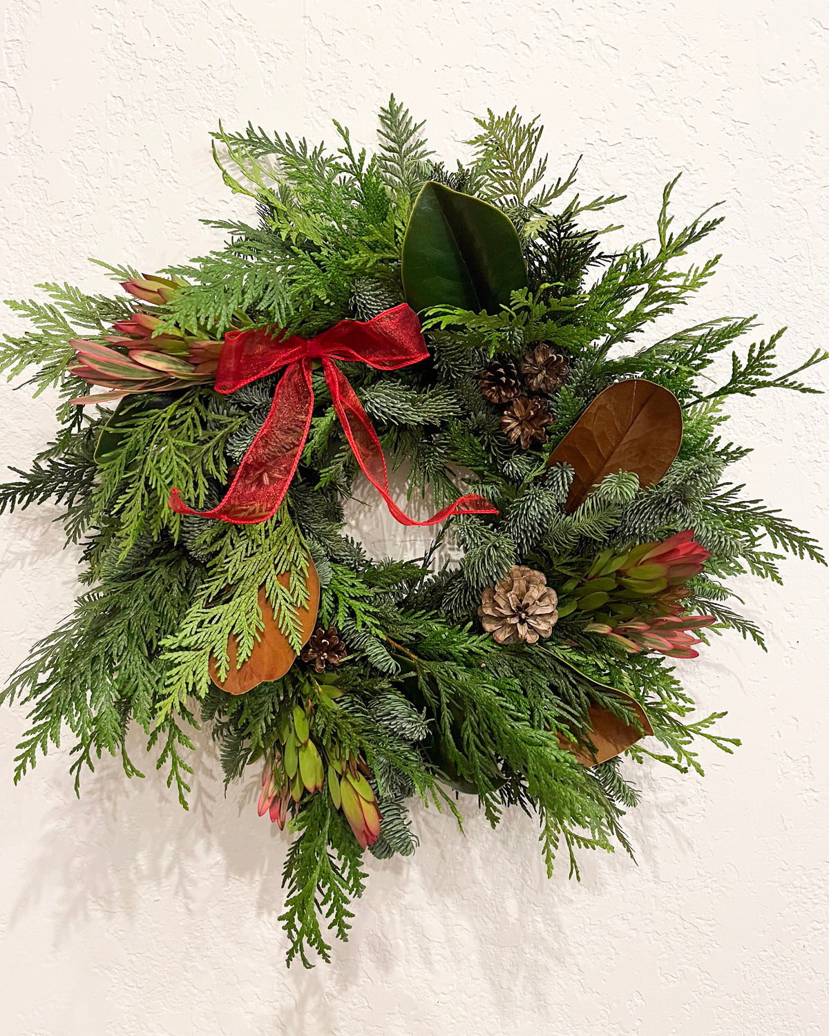 Green wreath with red ribbon and pinecones on a white background