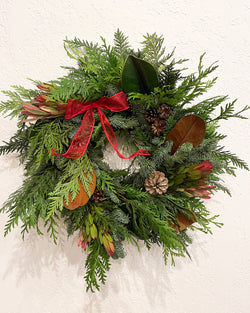 Green wreath with red ribbon and pinecones on a white background