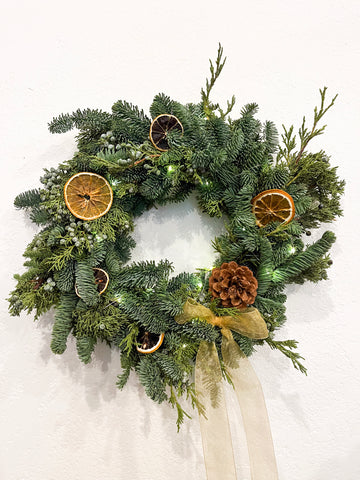 Christmas wreath with greenery, pinecones, and dried oranges on a white background