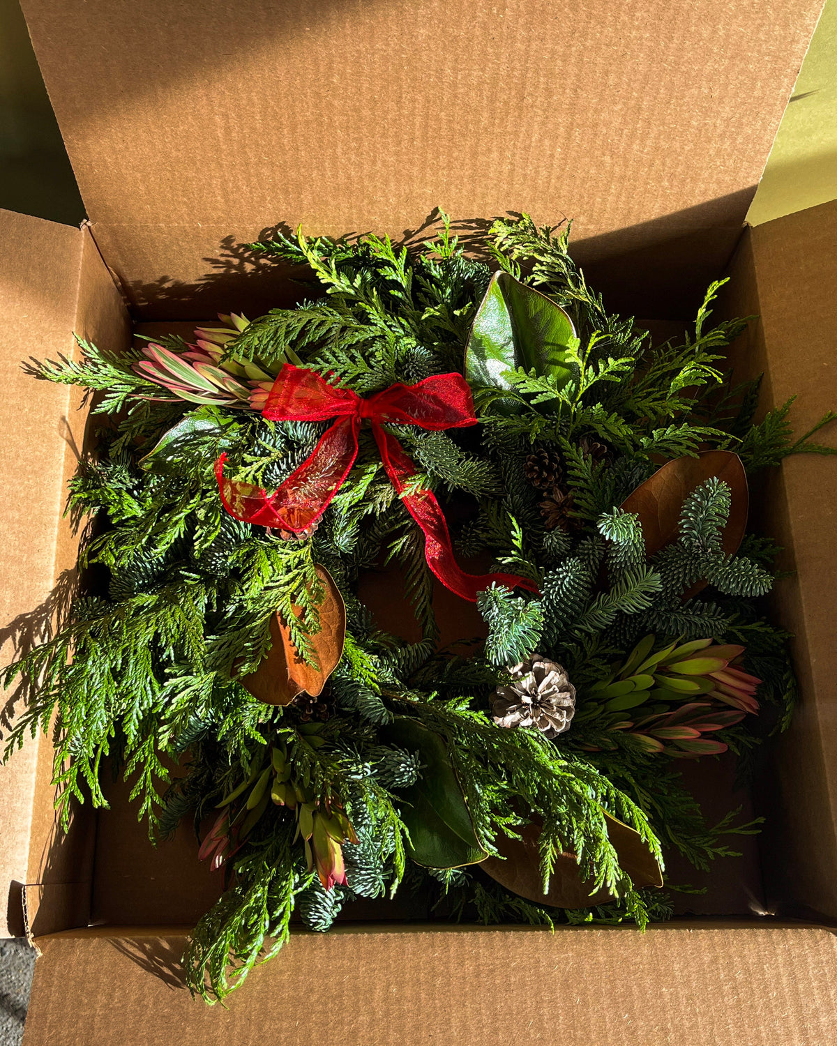 Green wreath with a red ribbon in an open cardboard box