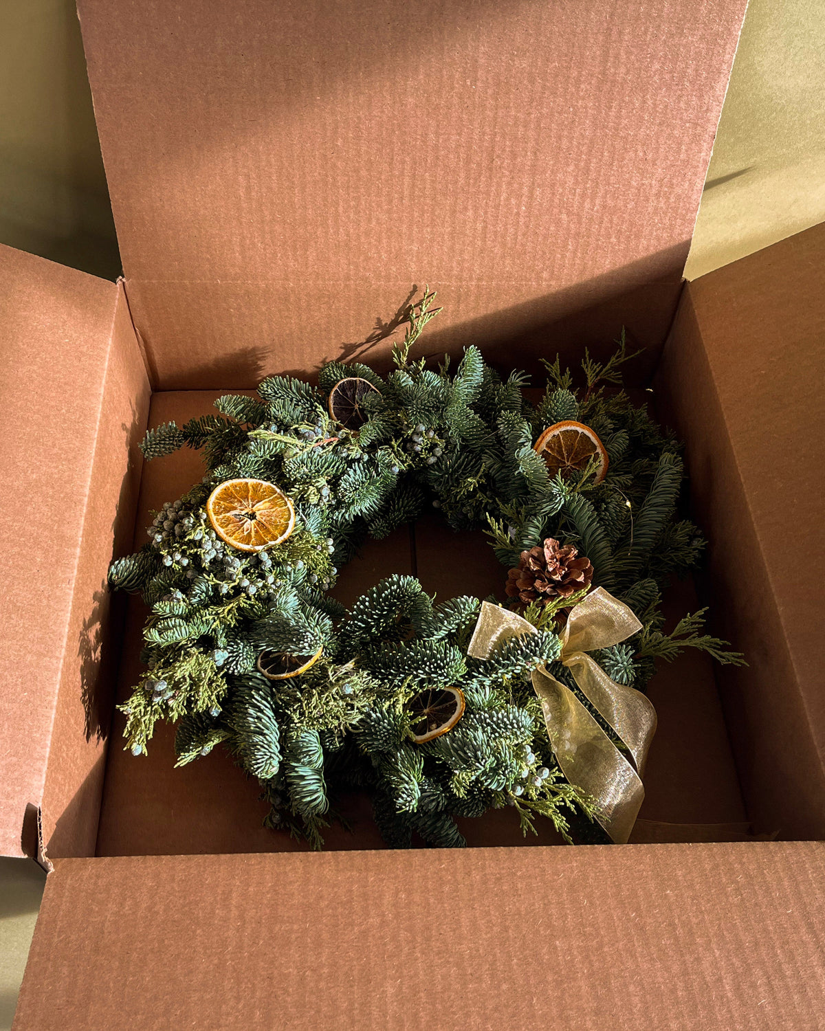 Christmas wreath with decorative elements inside an open cardboard box.