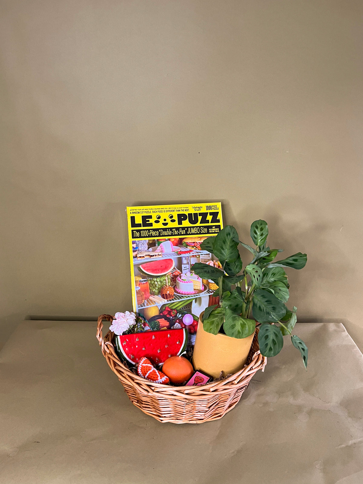 Basket with puzzle, potted plant, citrus candle, watermelon vase, citrus keychain, and matchbook on paper background. 