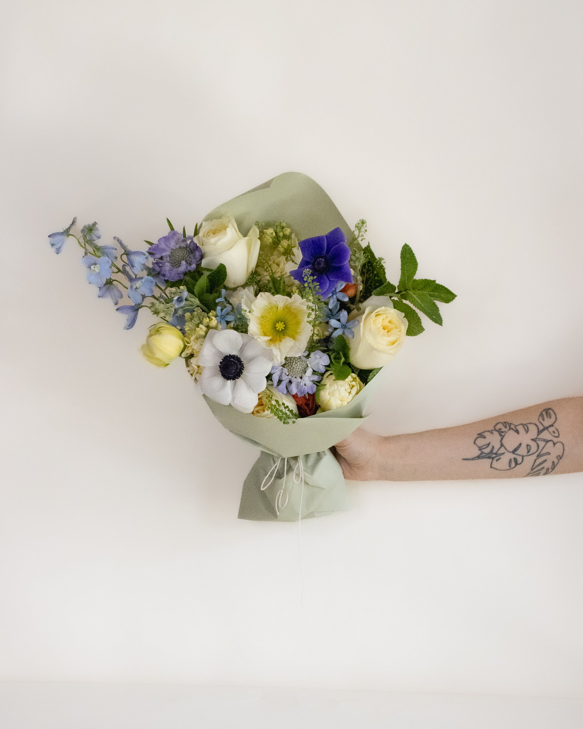 Bouquet of flowers held by a person with a tattoo on a light background