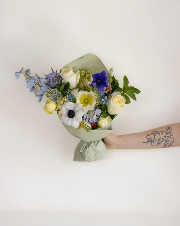 Bouquet of flowers held by a person with a tattoo on a light background