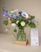 Arrangement of flowers in a clear vase on a wooden block with a bar of milk chocolate next to it.