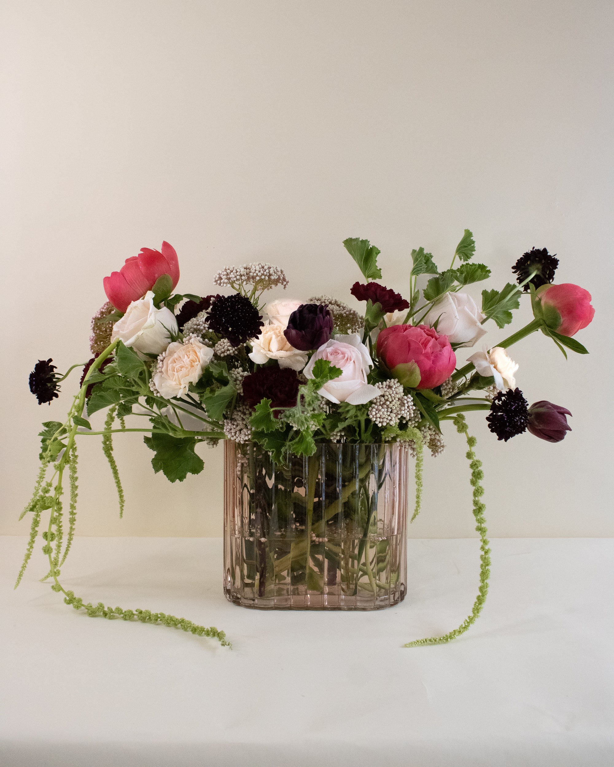 Luxe floral arrangement in a clear pink vase on a white surface with a light background