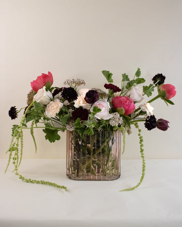 Luxe floral arrangement in a clear pink vase on a white surface with a light background