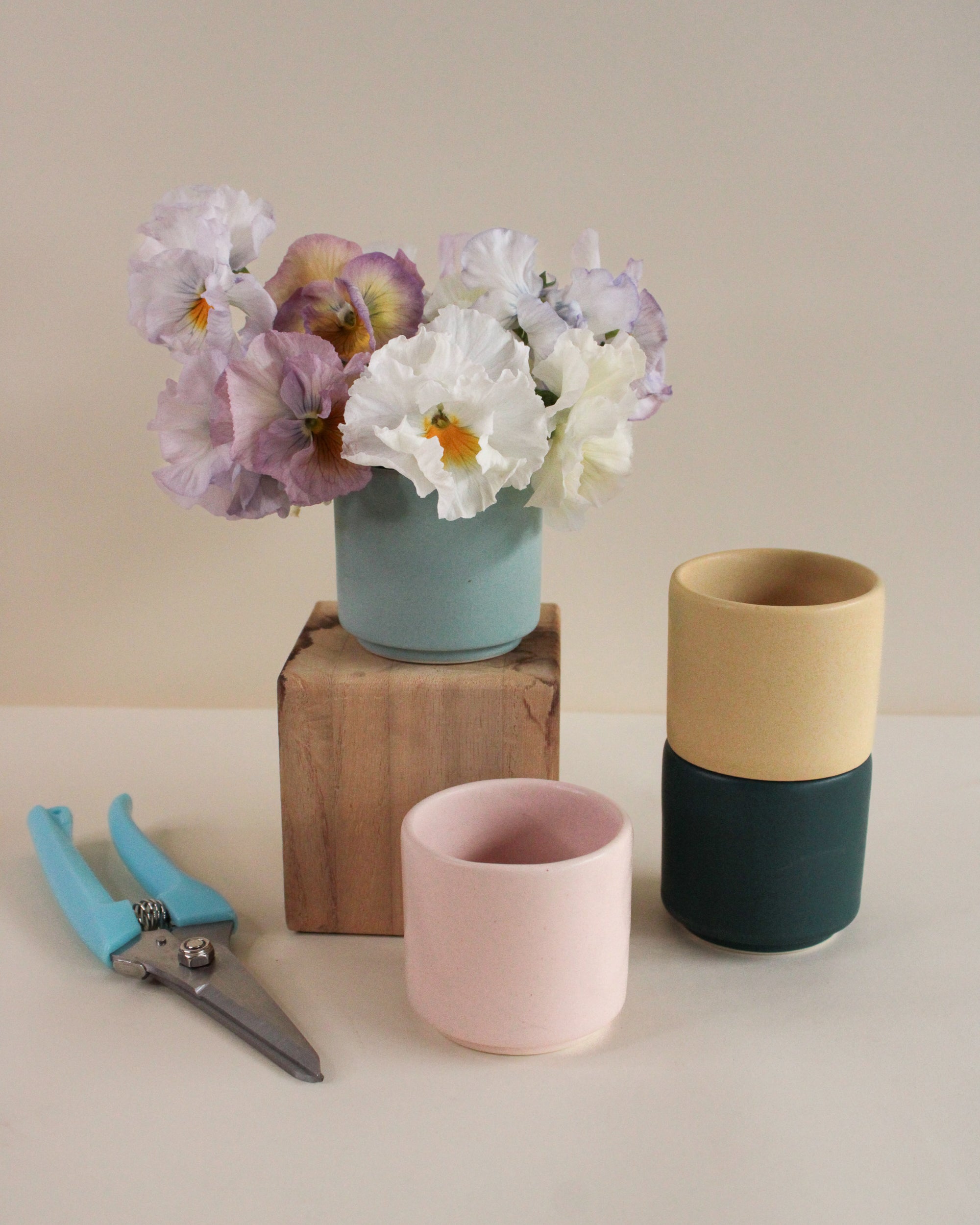 Three handmade ceramic vases with different color combinations on a neutral background, one with pansies.