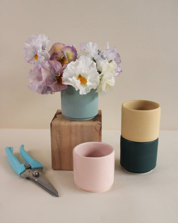 Three handmade ceramic vases with different color combinations on a neutral background, one with pansies.
