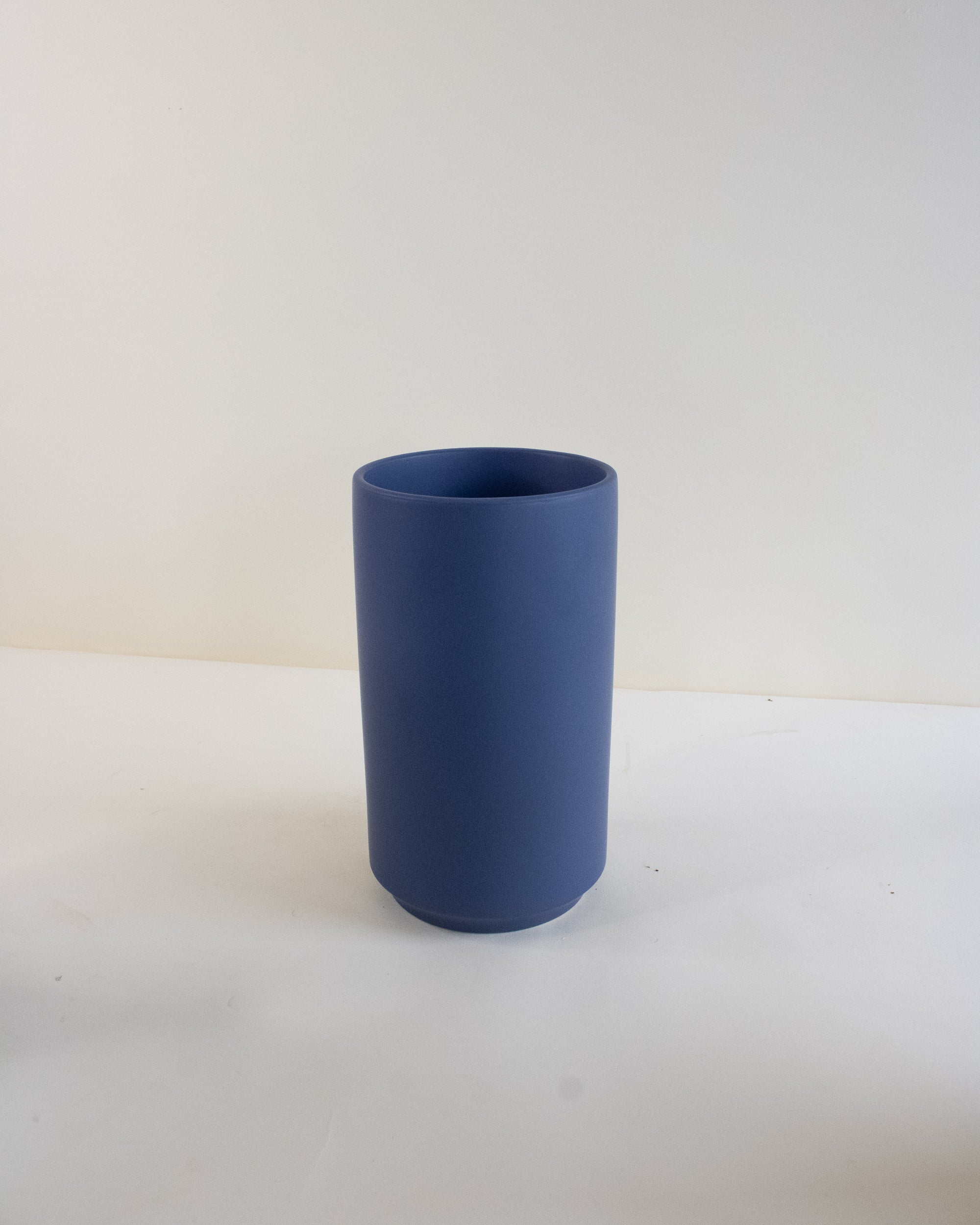 Blue cylindrical vase on a white surface with a light gray background