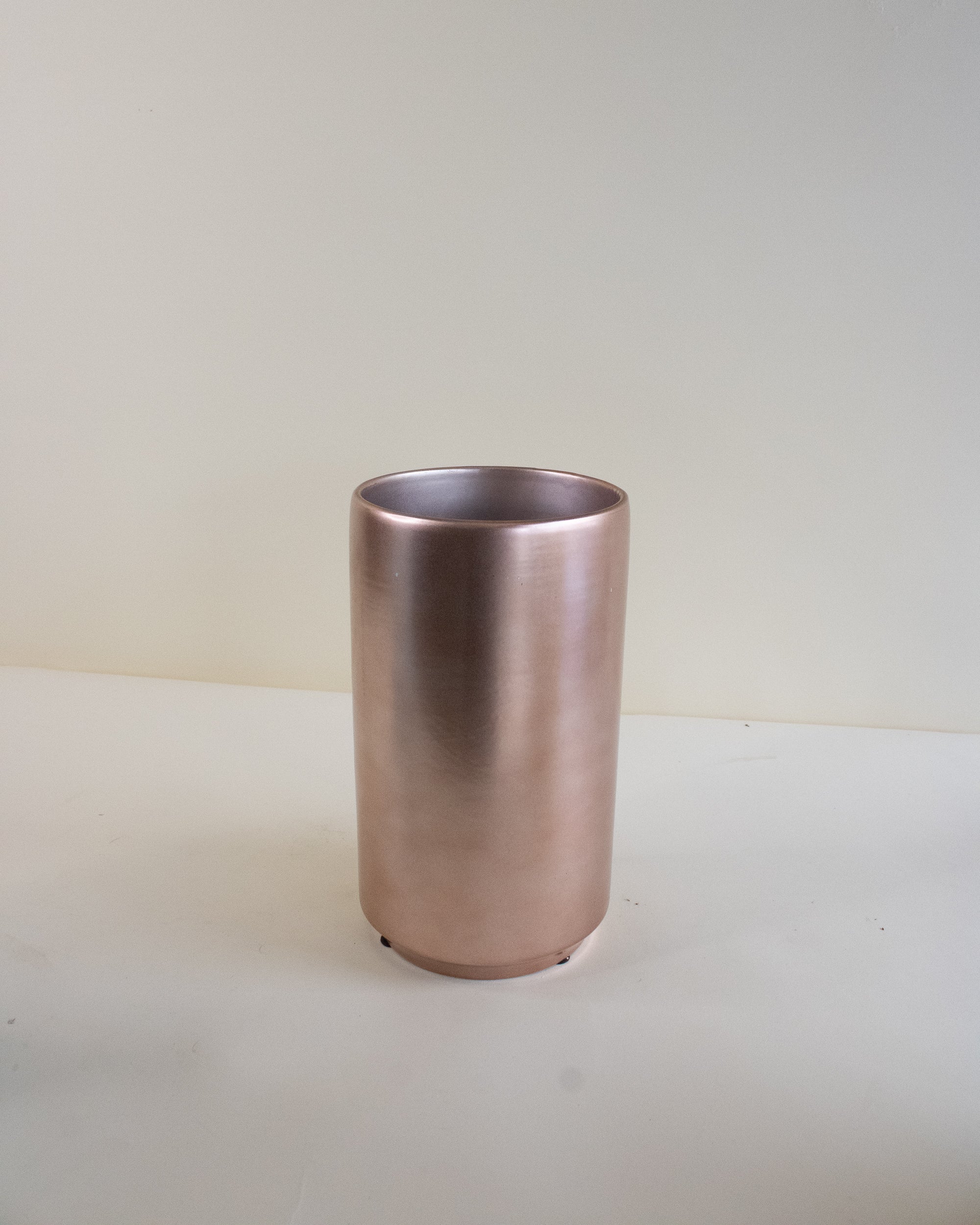 Rose gold ceramic vase on a white surface with a light grey background