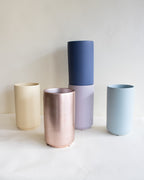 Five cylindrical vases in different colors on a white surface