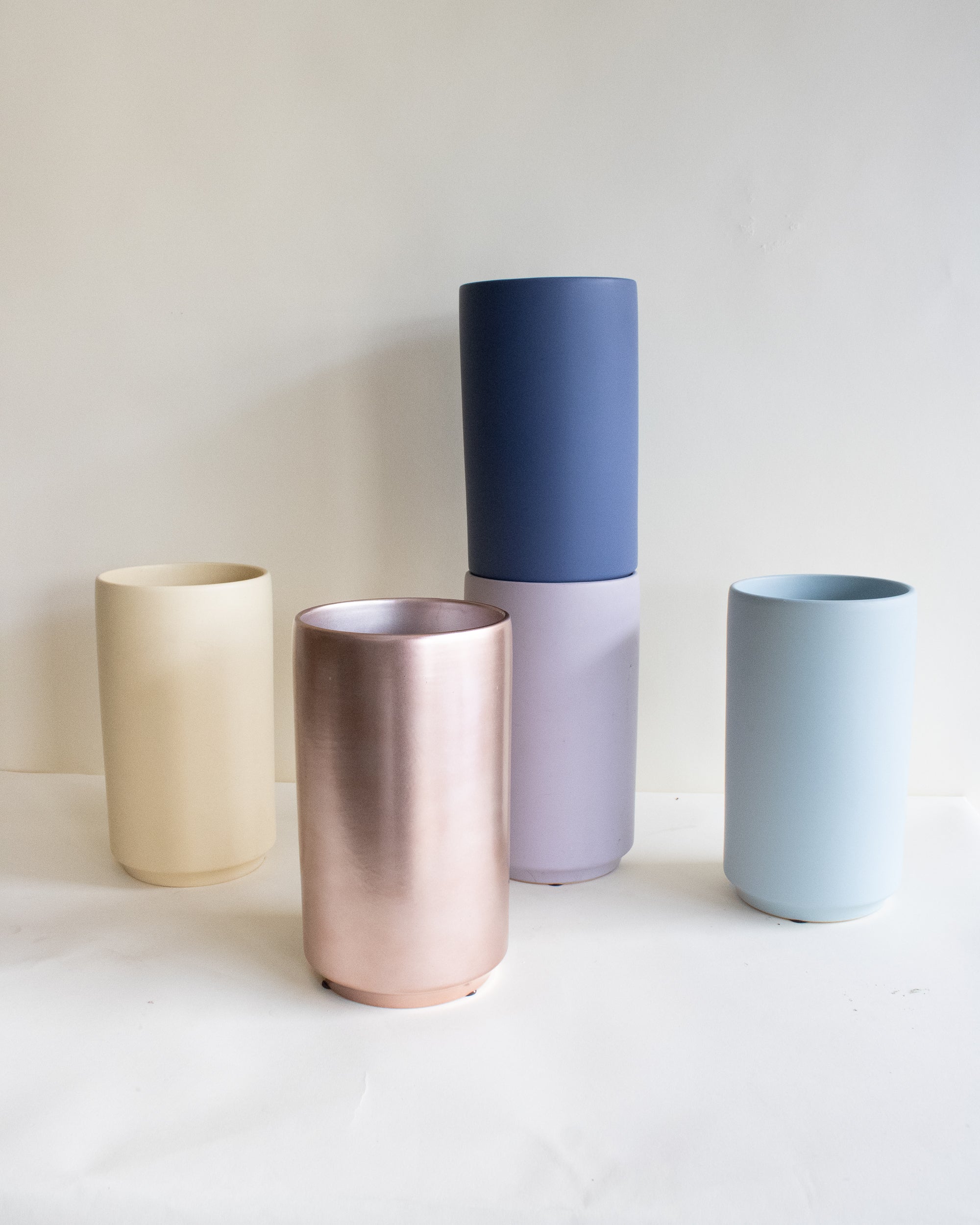 Five cylindrical vases in different colors on a white surface