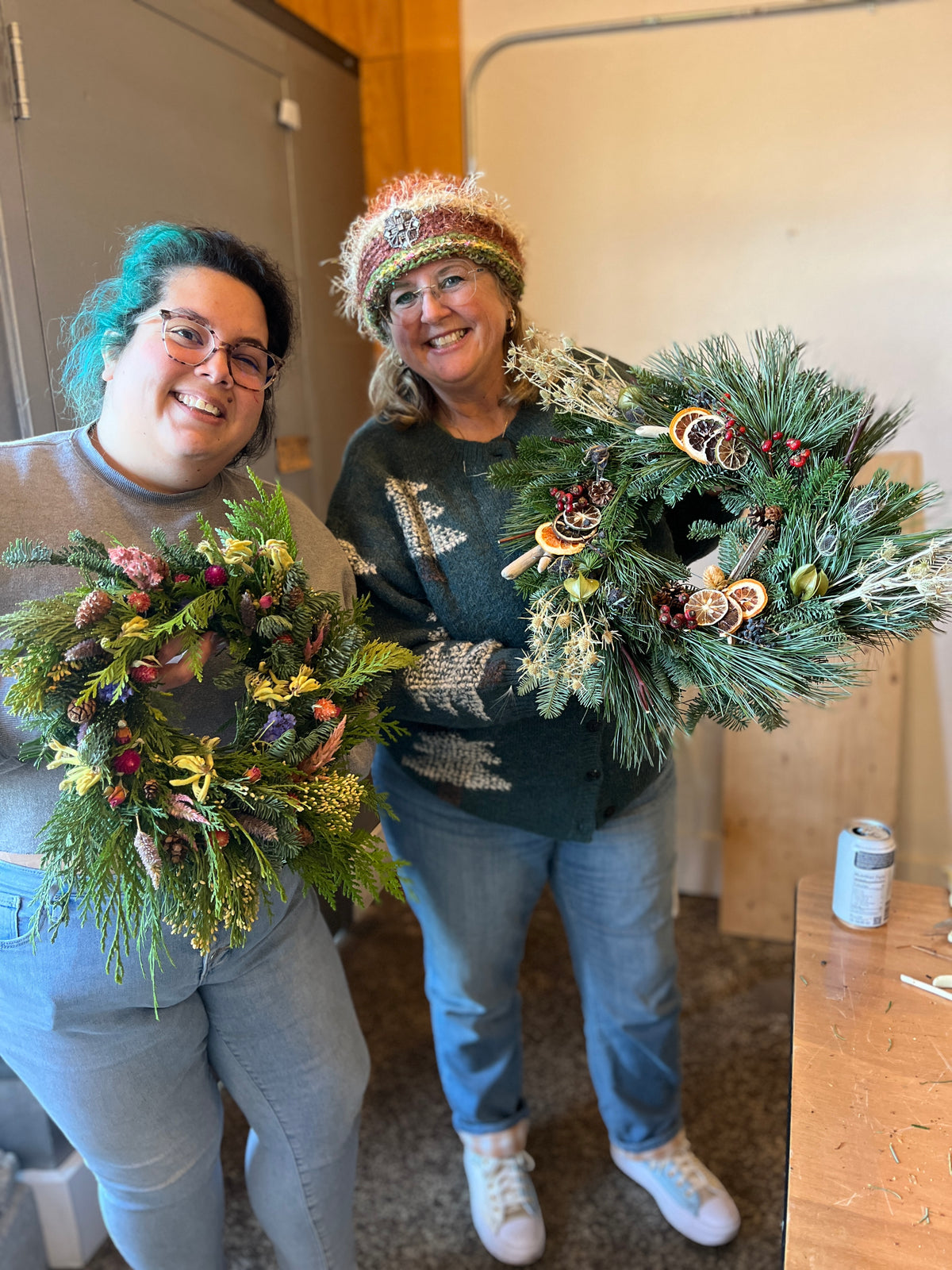 Two people holding Christmas wreaths indoors.