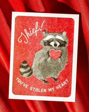 Card with a raccoon holding a heart and text on a red background