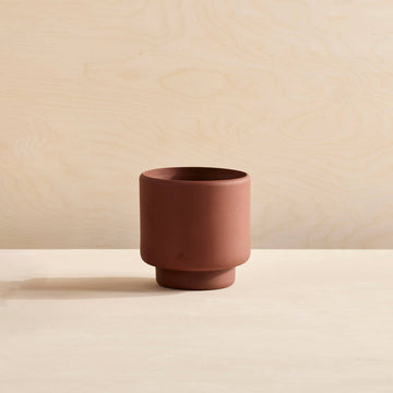red terra cotta pot with foot on bright plywood back drop