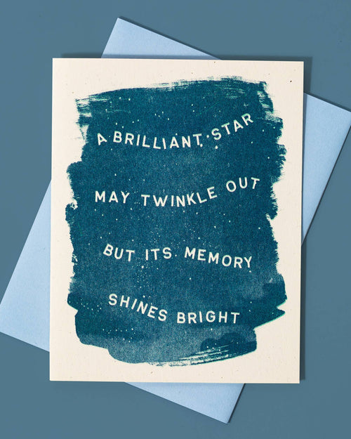 A Sympathy card with a blue abstract design and text that reads 'A BRILLIANT STAR MAY TWINKLE OUT BUT ITS MEMORY SHINES BRIGHT'. It is accompanied by a light blue envelope.
