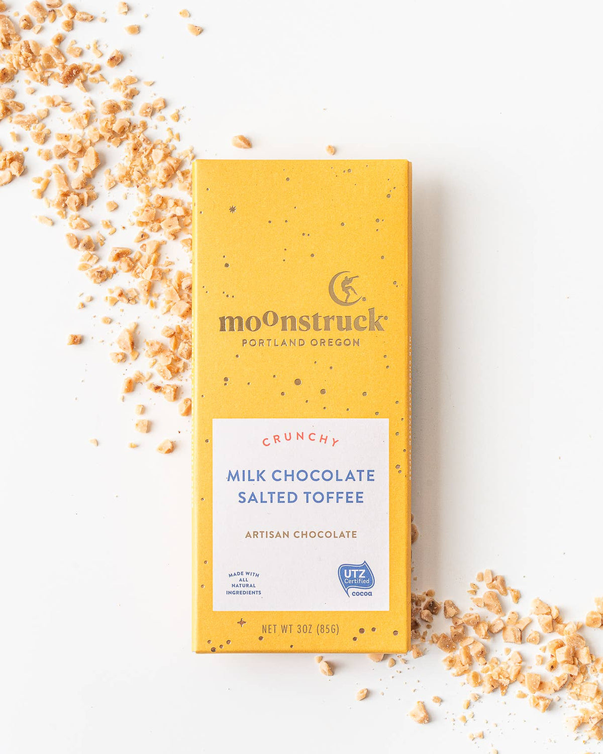 Moonstruck milk chocolate salted toffee bar with scattered toffee pieces on a white background