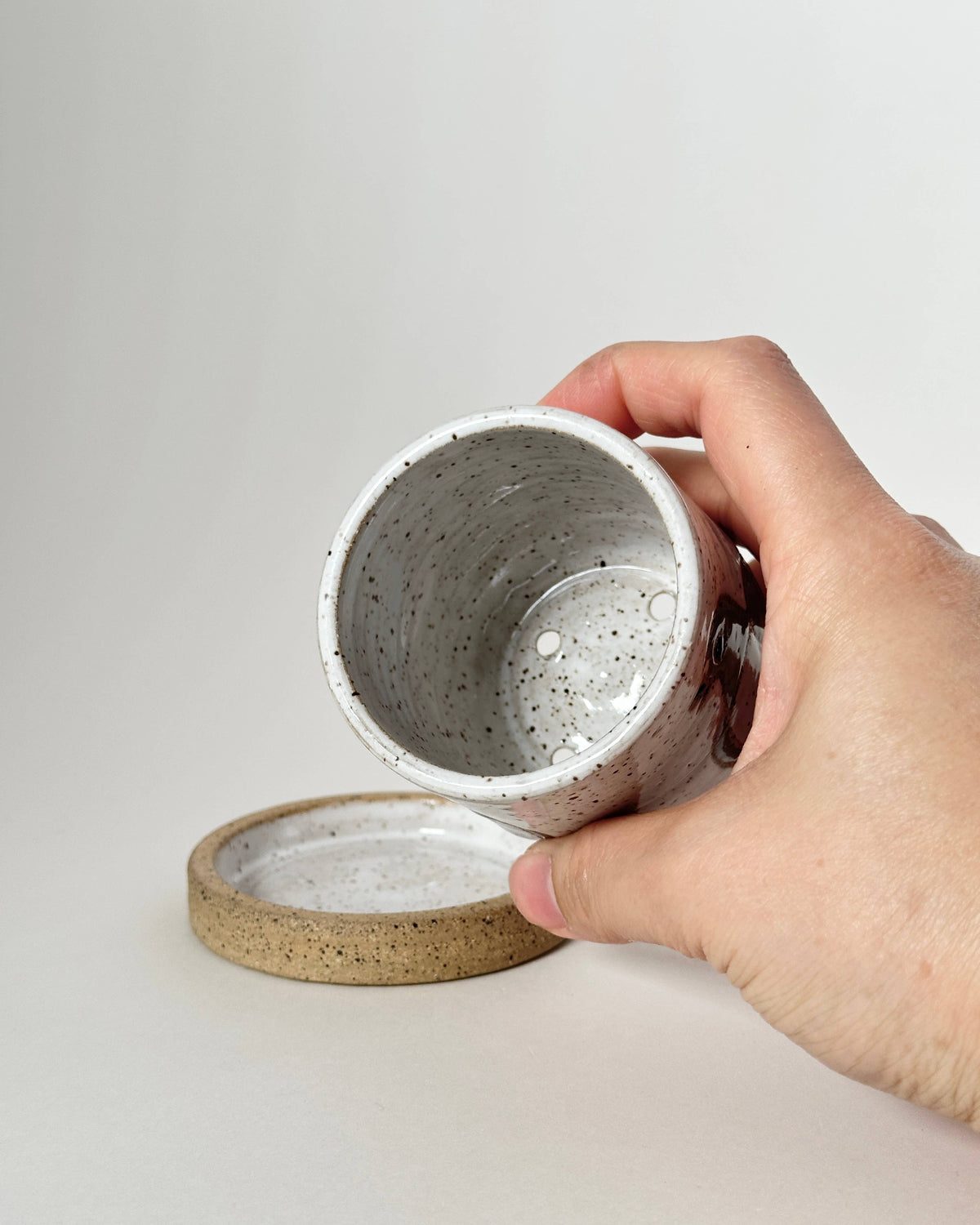Hand holding a concrete-like container with a matching lid on a light gray background
