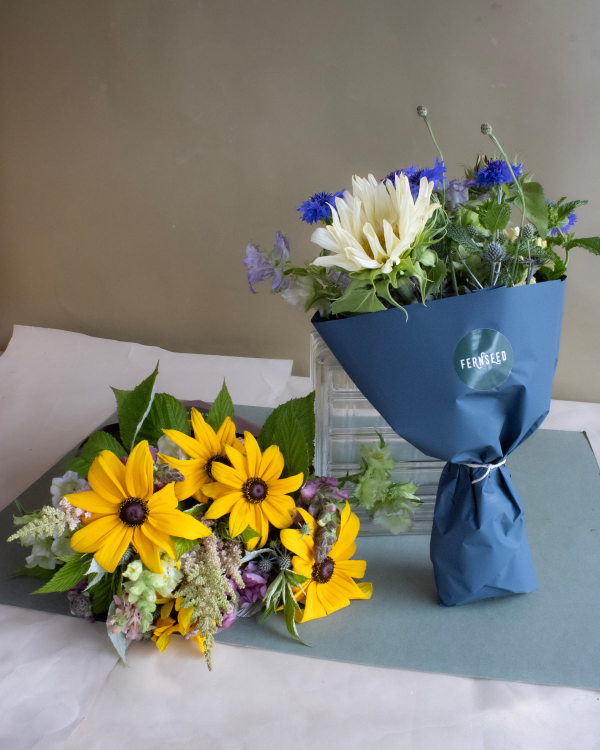 Two bouquets of flowers, one yellow and one with a mix of colors, featuring sunflowers, on a gray surface.