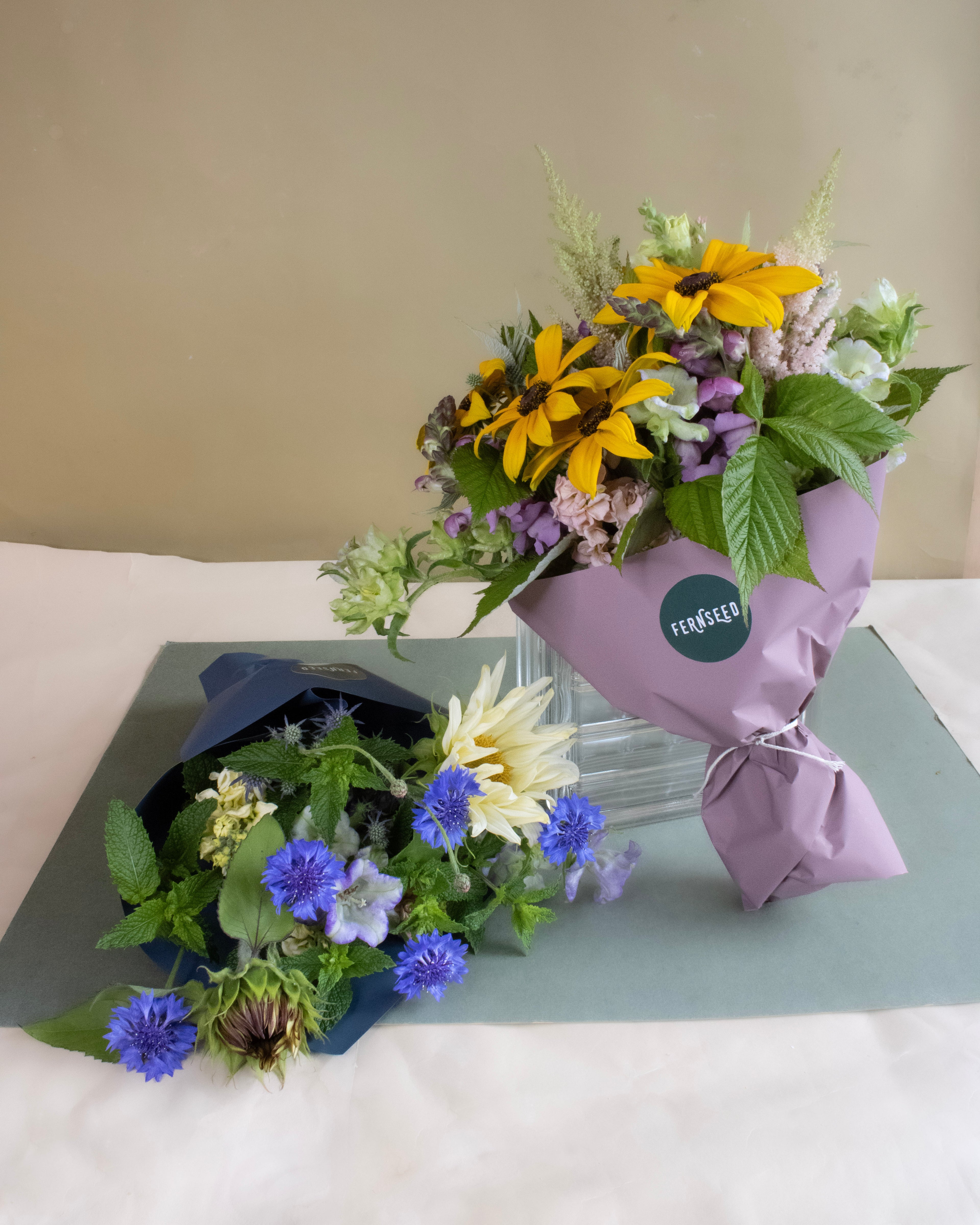 Two flower bouquets featuring sunflowers on a light surface with a neutral background