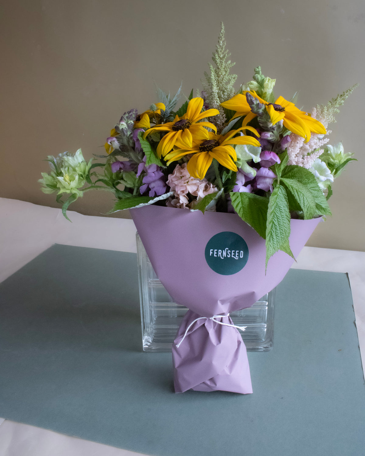 Bouquet of flowers wrapped in purple paper with a Fernseed label on a gray surface.