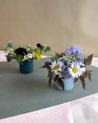 Two flower arrangements in small pots on a green tablecloth.
