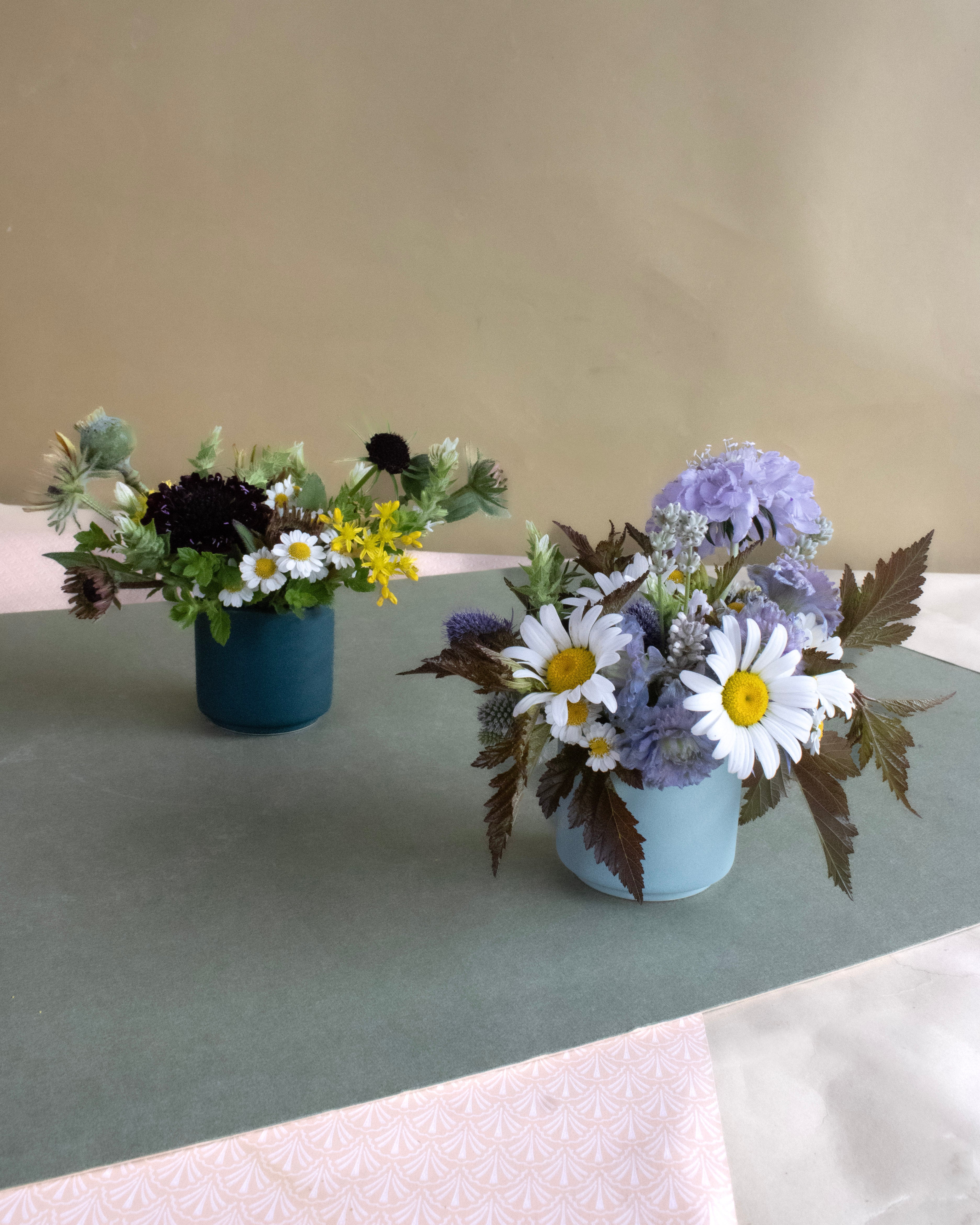 Two flower arrangements in small pots on a green tablecloth.