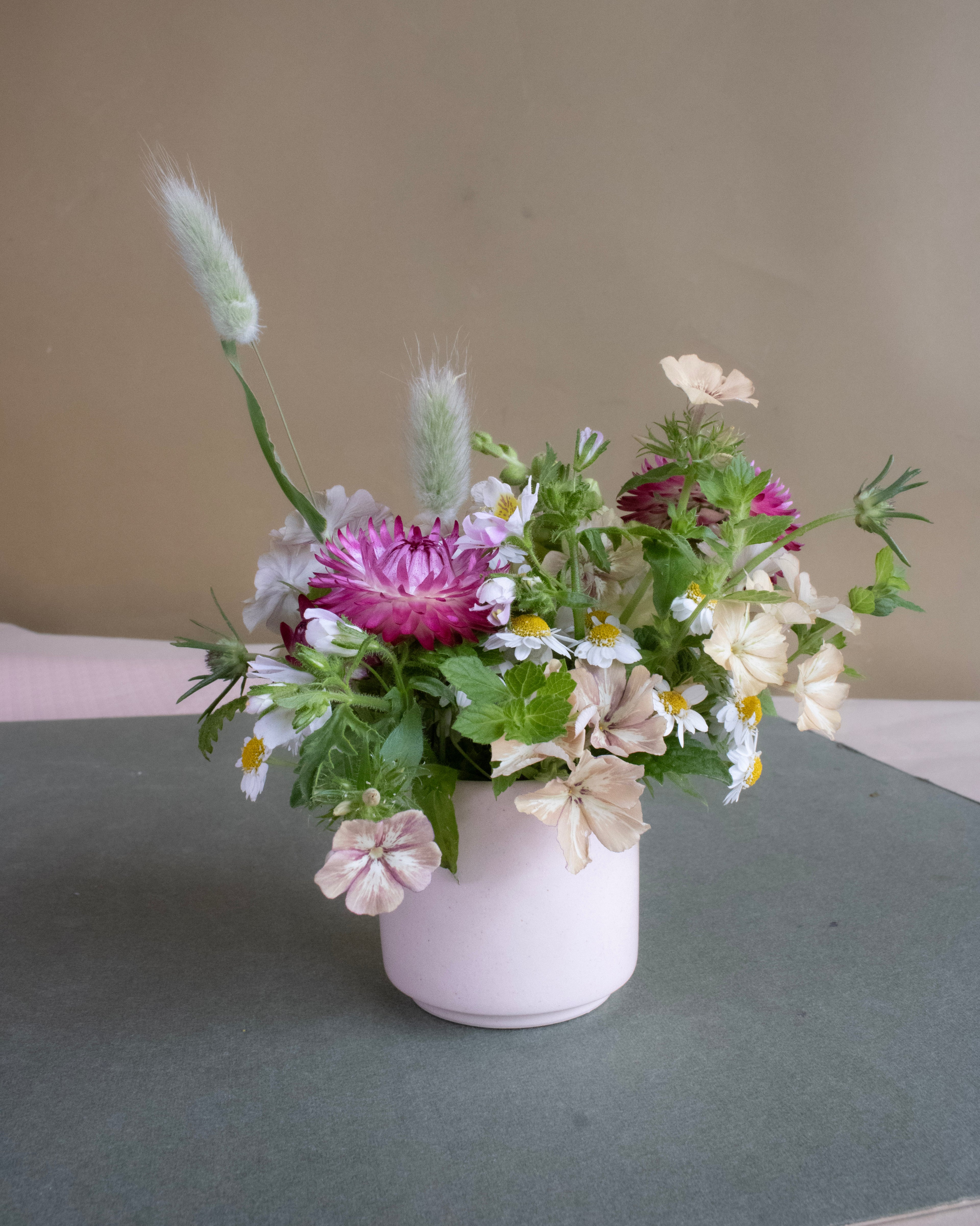 Small bouquet of flowers in a pink vase on a gray surface with a beige background
