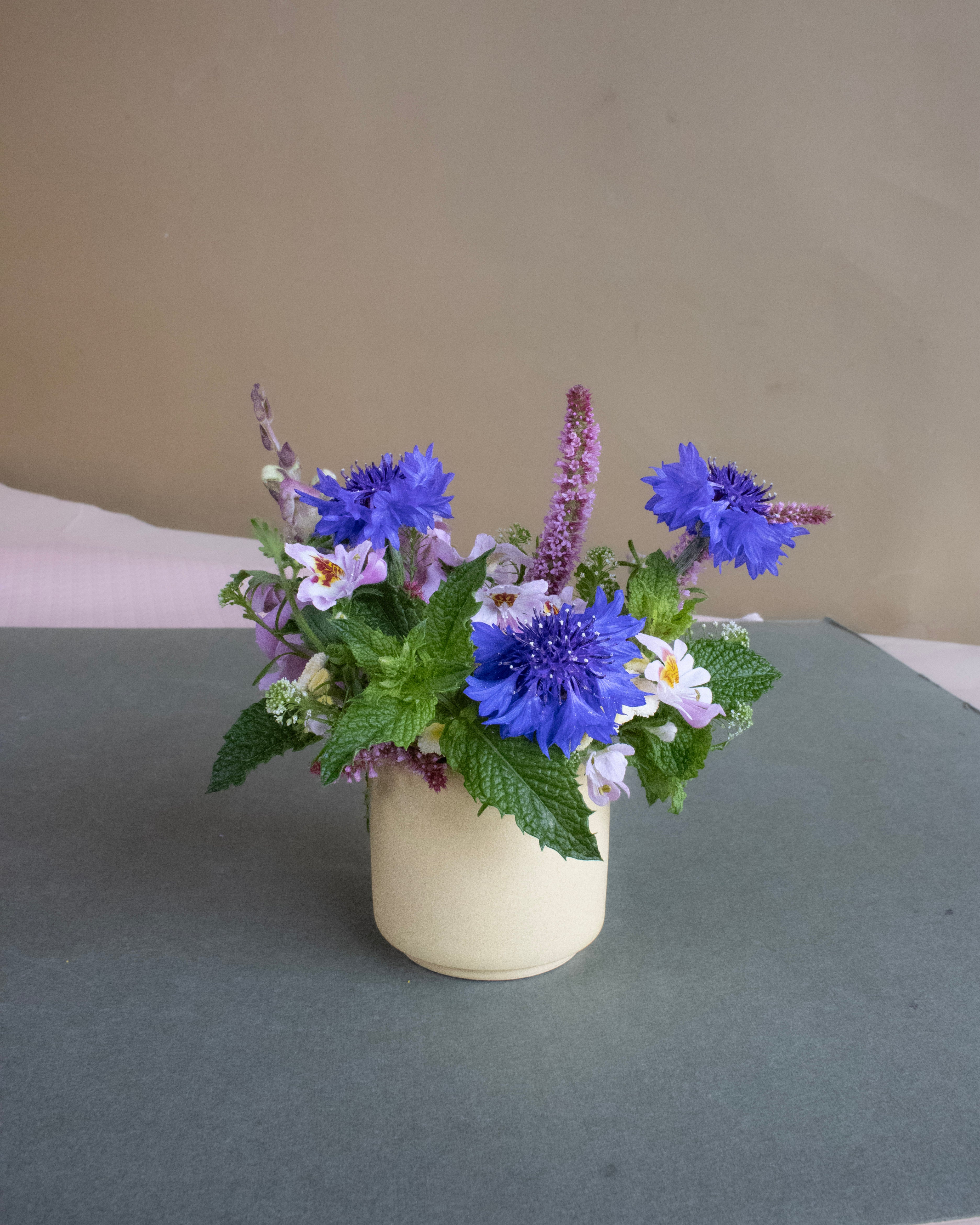 yellow vase with blue and purple flowers on a green gray surface