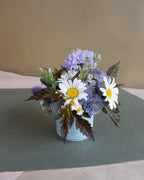 Floral arrangement with daisies and hydrangeas in a white vase on a green surface.