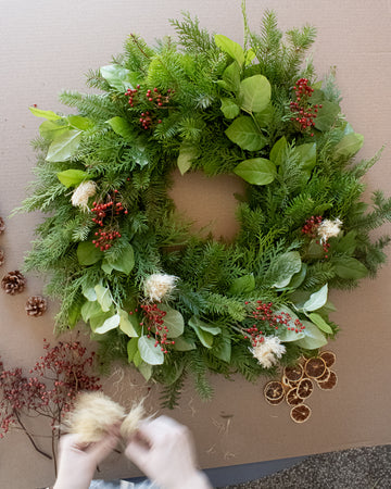 A decorated evergreen wreath with a pre-made wire-frame structure, adorned with a variety of dried botanicals including flowers, grasses, and berries.